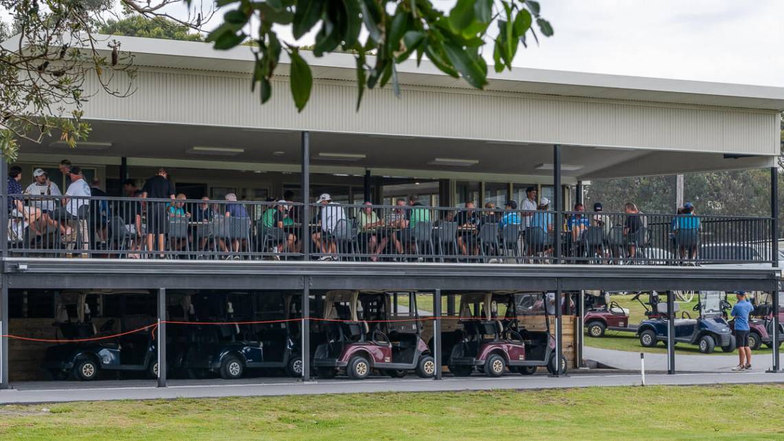 Members and guests gathered on the upper-level clubhouse balcony overlooking a row of golf carts parked below, enjoying a tournament event day at the club.