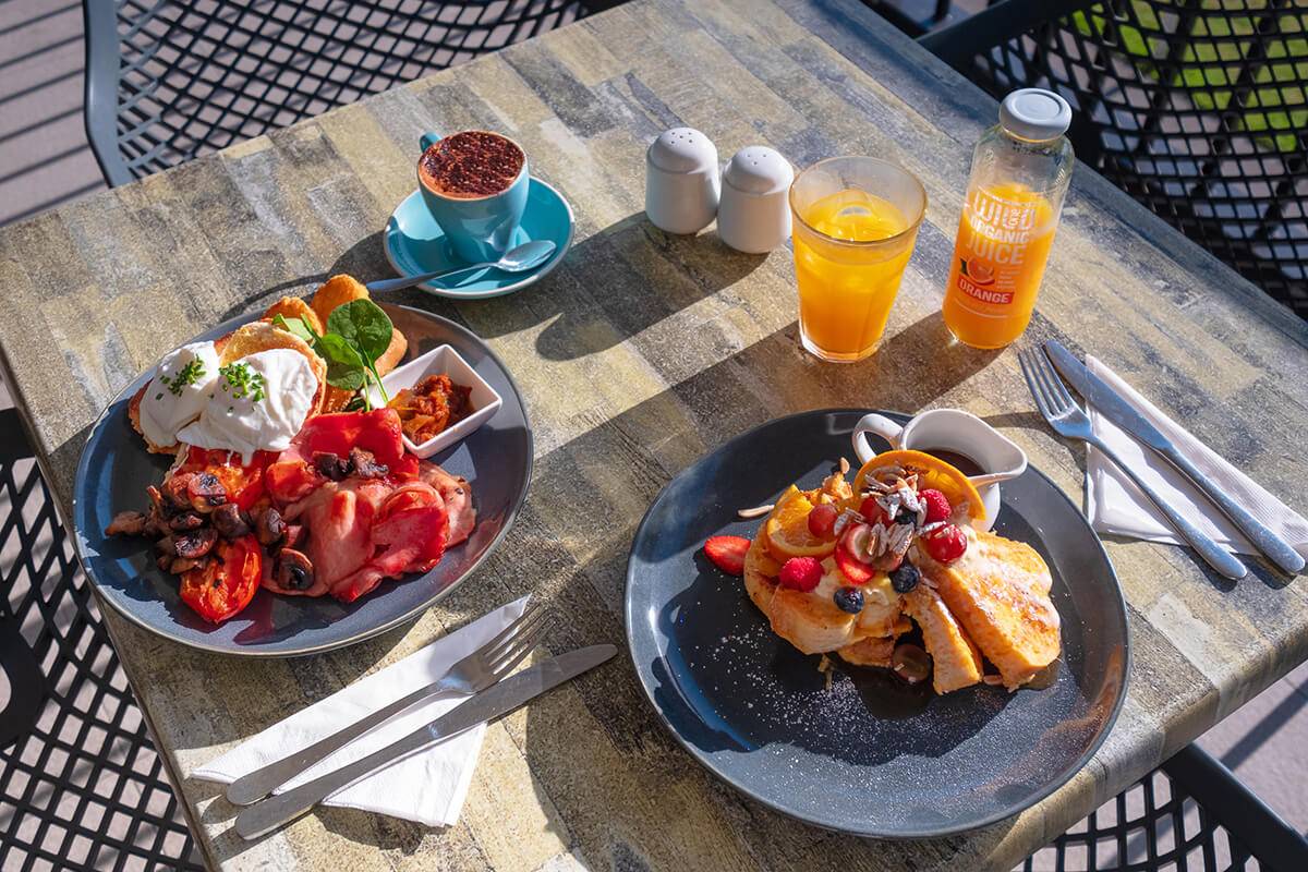 Breakfast dishes with bacon, eggs, French toast, and fresh fruit served outdoors at Shoalhaven Heads Golf Club Restaurant.